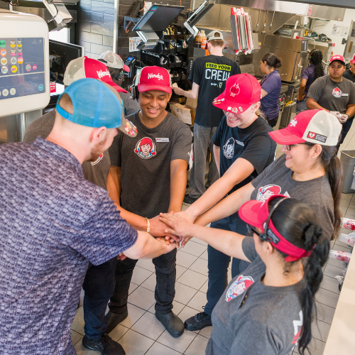 Wendy's employees huddle in a circle with their hands together.