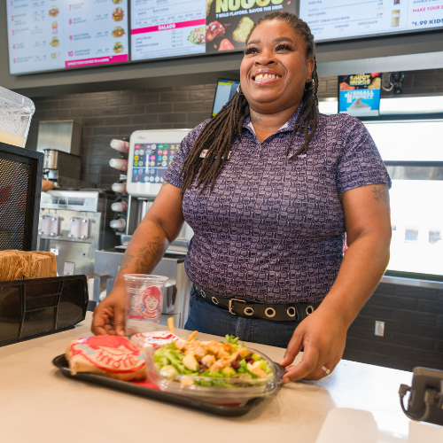 Wendy's employee smiles as she sets a tray of food on the counter.